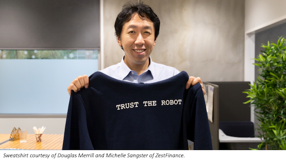 Andrew Ng holding a sweatshirt that says "Trust the robot"